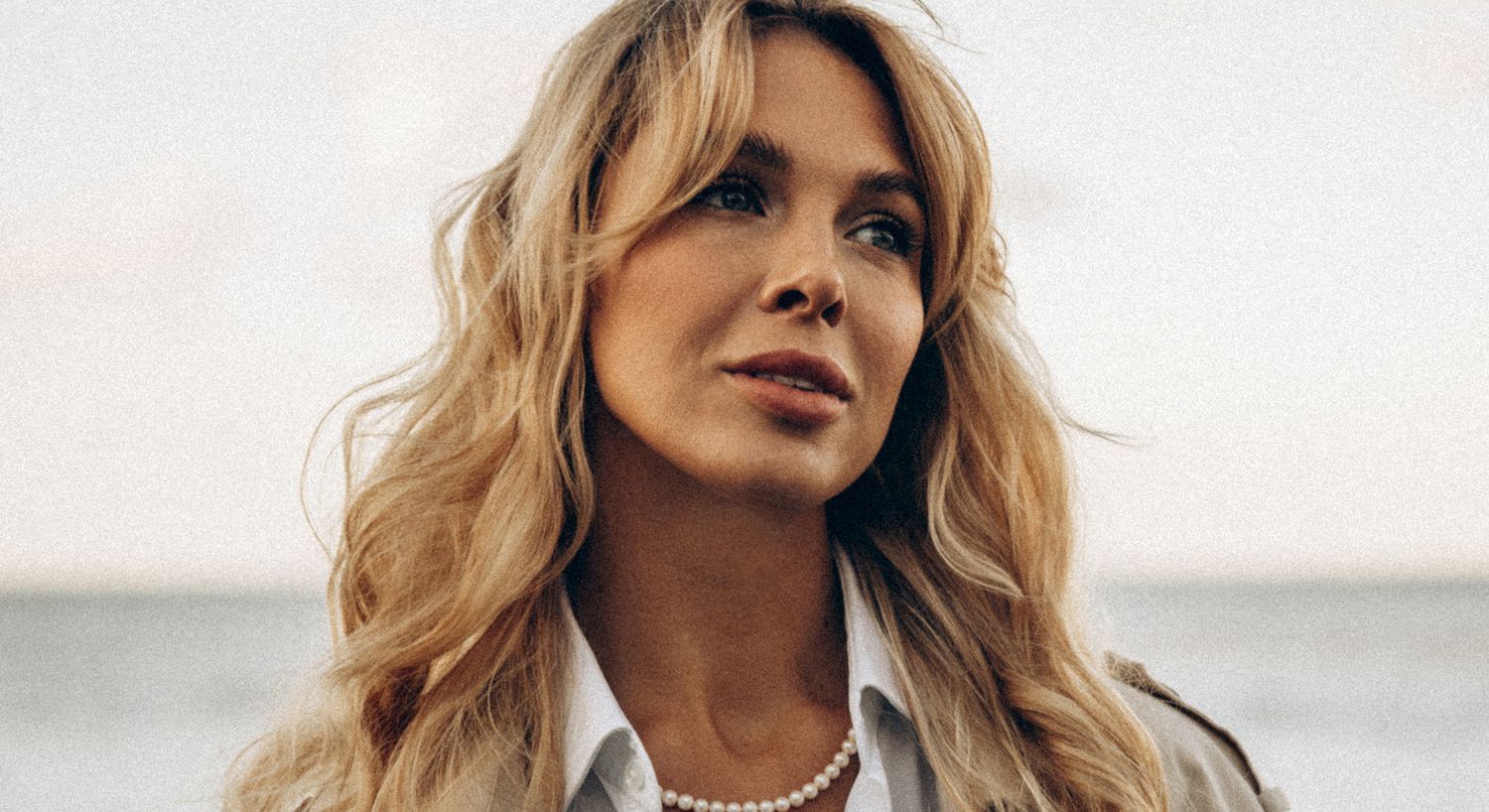 Smiling woman with flowing hair by the beach.