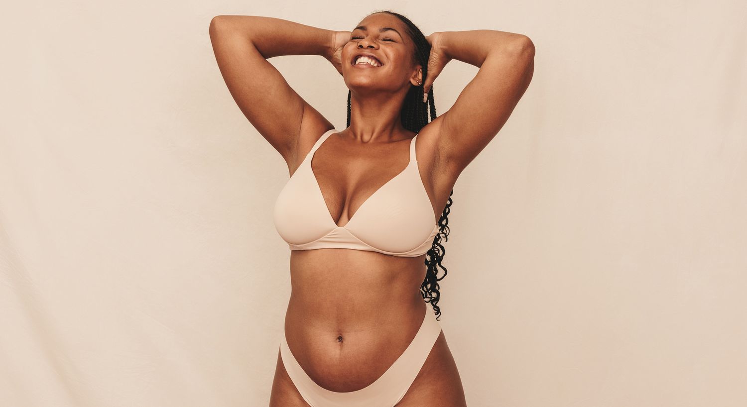 Smiling person in nude lingerie against neutral background.