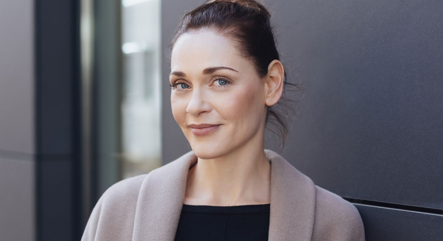 Smiling woman in stylish coat against dark wall.
